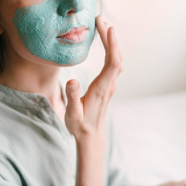 Young woman applies a rejuvenating facial mask indoors for skin care and relaxation.